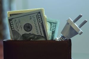 A wallet with money and an electrical plug coming out of it.